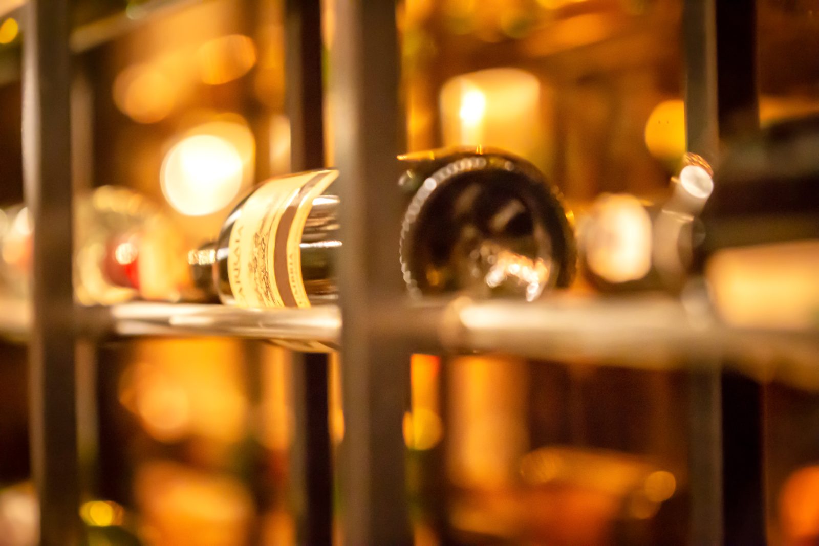 Bouteilles présentées sur un casier métallique éclairé dans une cave à vin contemporaine.